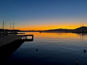 Una marina con imbarcazioni ormeggiate, acque calme e un tramonto sullo sfondo.