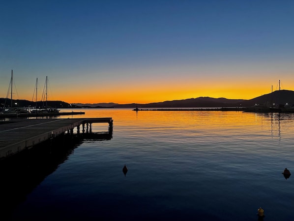 A marina with boats docked, calm water, and a sunset in the background.