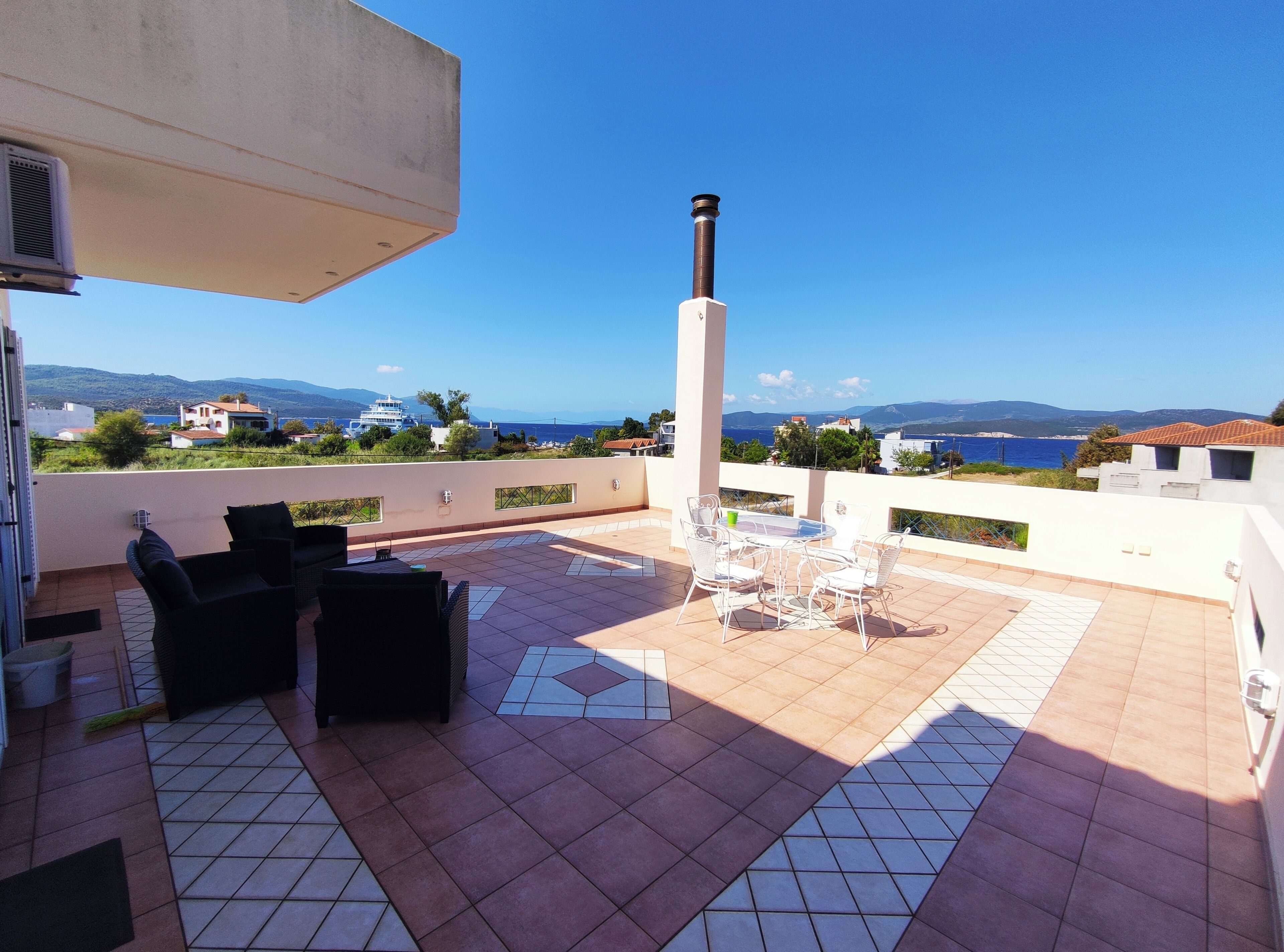 Una terrazza con mobili da esterno, un camino e vista sul mare e sulle colline in lontananza.