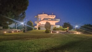 A modern multi-story house with a flat roof and large windows, surrounded by a well-maintained lawn and trees.