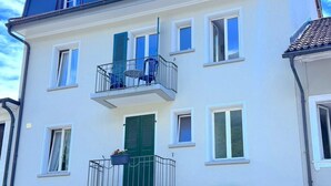 Un immeuble résidentiel à plusieurs étages, doté de balcons, de volets verts et d’une porte de garage.
