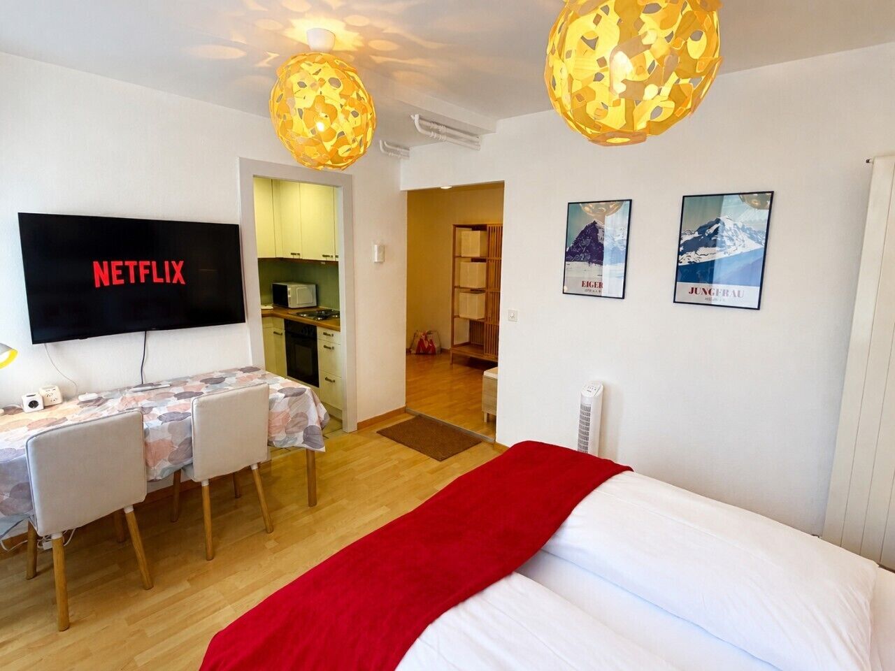 Una habitación de hotel con cama, un escritorio con sillas, un televisor y dos lámparas fijadas a la pared.