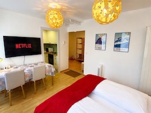 A hotel room with a bed, a desk with chairs, a TV, and two wall-mounted lamps.