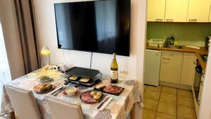 Ein Essbereich mit einem Tisch für zwei Personen, einem Fernseher darüber und einer Küche im Hintergrund.