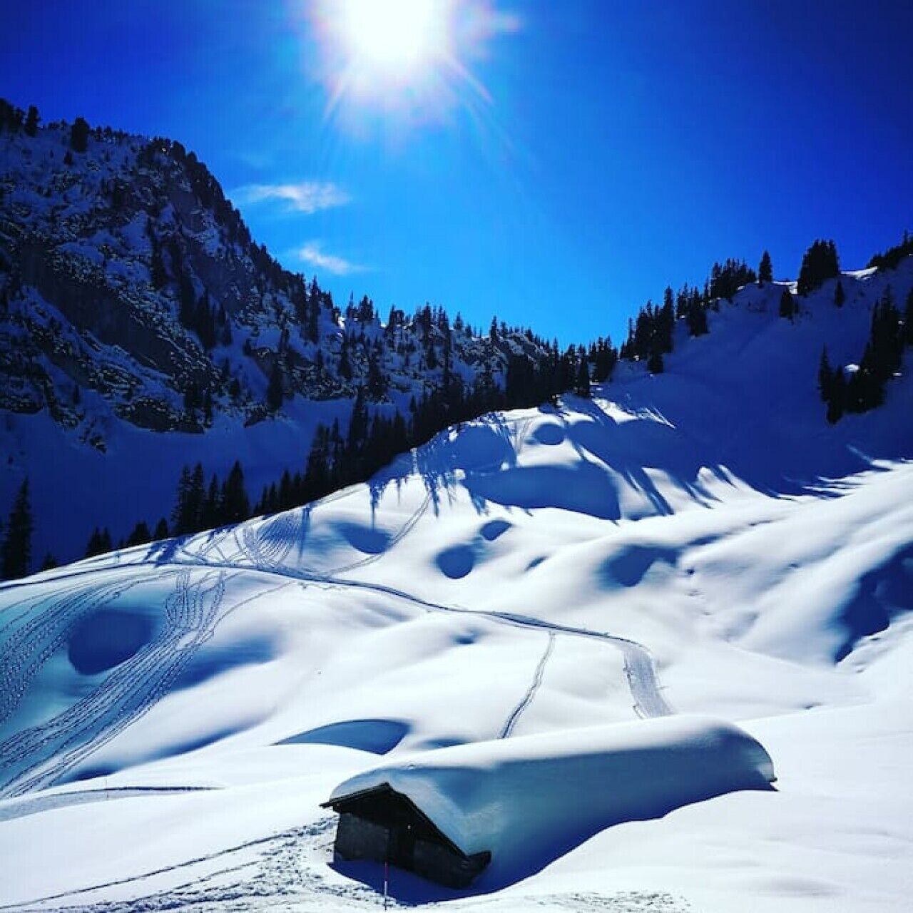 A snow-covered mountain landscape with a clear sky and a sun shining.