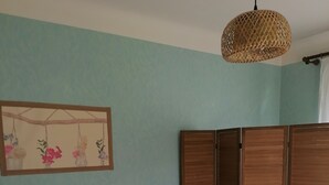 Un dormitori amb un llit, una taula de nit, una làmpada penjant, un armari i una pintura mural.