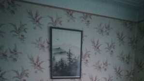 Una habitació amb paper pintat, un armari de fusta i un quadre al mur.