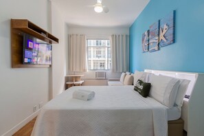 Una habitación de hotel con cama, televisión, ventana con cortinas, escritorio y un cuadro en la pared.
