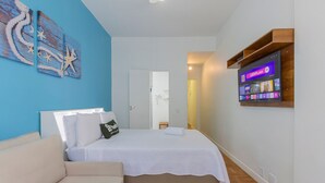 Une chambre à coucher comprenant un lit, un canapé, un téléviseur fixé au mur et une porte donnant sur une autre pièce.