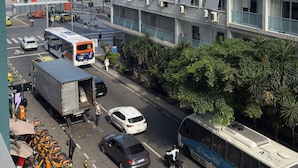 Un immeuble à plusieurs étages doté de balcons, une vue sur la rue avec des véhicules, et une plage en arrière-plan.