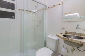 Ein Badezimmer mit Duschkabine aus Glas, Toilette, Waschbecken mit Marmorplatte und Handtuchhalter.