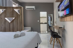 Ein Hotelzimmer mit Bett, Schreibtisch, Stuhl, Fernseher und Klimaanlage.