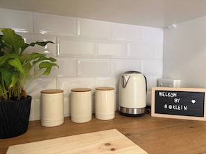 A kitchen with white tiles, a coffee maker, three sugar containers, a potted plant, and a welcome sign. - Accommodation 8 Klein Straat Green (Paarl)