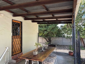 A covered patio with a wooden table, a potted plant, and a door with a metal grille. - Accommodation 8 Klein Straat Green (Paarl)