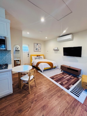 Ein kleines Hotelzimmer mit Bett, Fernseher, Schreibtisch mit Stuhl, einem kleinen Tisch und einer Küchenzeile.