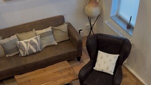 Una sala de estar con un sofá marrón, un sillón negro, una mesa de centro de madera y un pequeño otoman.