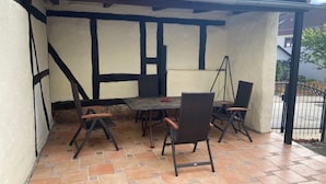 Un patio techado con una mesa y sillas, piso de baldosas y barandilla de metal negro.