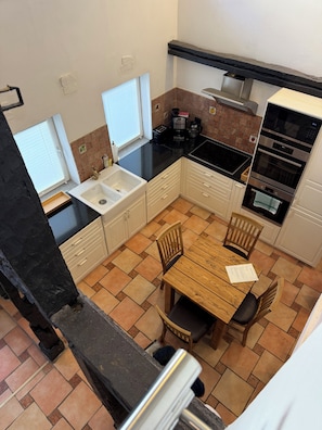 A compact kitchen with a sink, stove, and dining area, featuring a tiled backsplash and a window. - Vacation home with ambience at the Hofgeismar town hall (Hofgeismar)