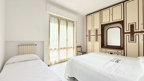 A bedroom with two beds, a large window with curtains, a radiator, and a wardrobe with geometric patterns. - SE267 – Senigallia, two-bedroom apartment 300 metres from the sea (Senigallia)