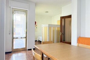 Un coin repas avec une table et des chaises en bois, une porte coulissante et une vue sur une pièce comprenant un lit et une fenêtre.