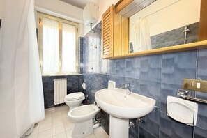 Une salle de bain comprenant des toilettes, un bidet et un lavabo, avec une fenêtre et un rideau de douche.