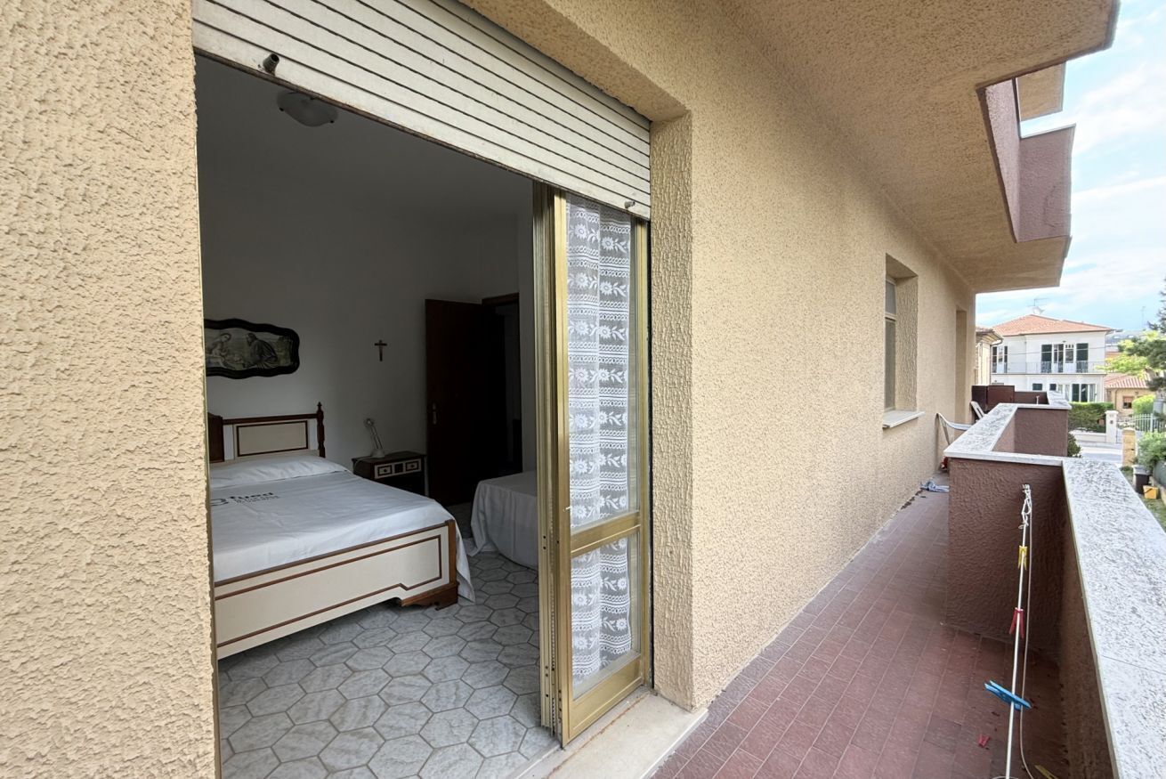 Ein Zimmer mit einem Bett, einem Fenster mit gemusterten Vorhängen und einem Balkon mit Geländer.