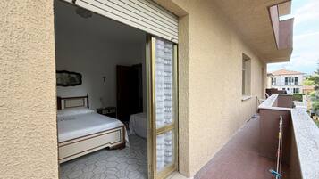 Ein Zimmer mit einem Bett, einem Fenster mit gemusterten Vorhängen und einem Balkon mit Geländer.