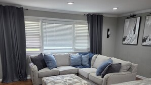 Ein modernes Wohnzimmer mit Ecksofa, Hocker und einer Kücheninsel aus Marmor.