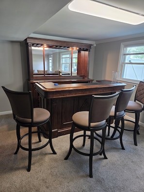 A bar area with a wooden counter, four barstools, and a large mirror.