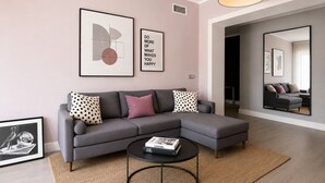 Ein modernes Wohnzimmer mit einem grauen Ecksofa, einem runden Couchtisch und gerahmten Kunstwerken an der Wand.