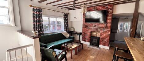 Una sala de estar acogedora con un sofá verde, vigas de madera, chimenea y un televisor montado encima.