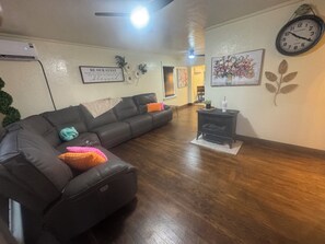 A living room with a sectional sofa, a small table with a plant, a clock, and a wall with a framed quote. - Pet Friendly  Sleeps 6  Fenced Yard  Patio (Elk City)