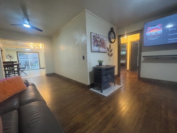 A living room with a black leather sofa, a fireplace, a clock, and a television displaying 'Master of Puppets.'