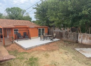 Une maison avec un patio, une balançoire et une cour arrière clôturée.