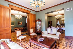 A spacious room with a large wooden cabinet, a chandelier, and a dining area with chairs and a table.