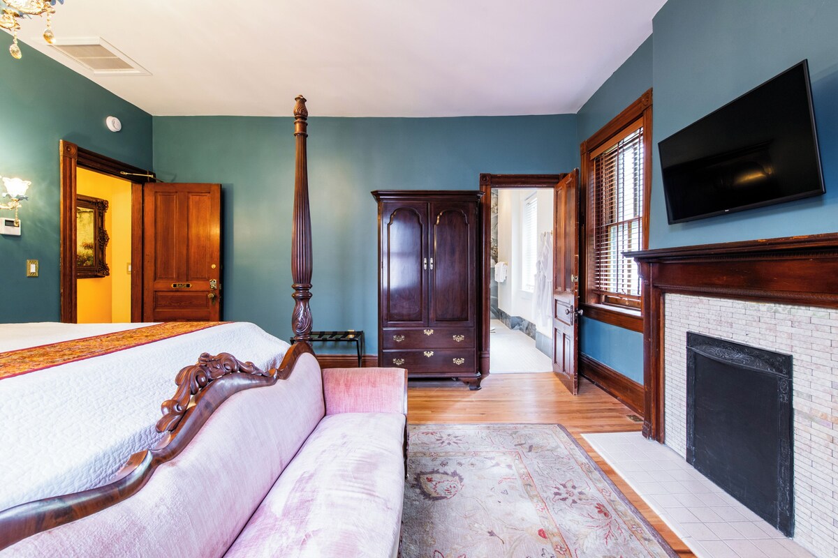Une chambre à coucher comprenant un lit, un coin salon avec un canapé, une armoire, une cheminée et un téléviseur.