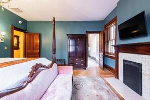 Un dormitorio con cama, zona de estar con sofá, armario, chimenea y televisor.
