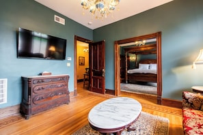 A room with a large flat-screen TV, a wooden dresser, a marble table, and a bed with a canopy. - Victorian Harvest (Louisville)