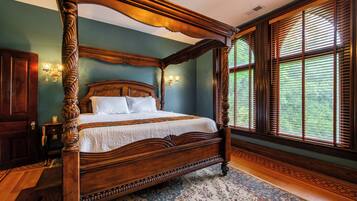 Una cama con dosel de madera, un tapete estampado con motivos florales y un ventanal con persianas.