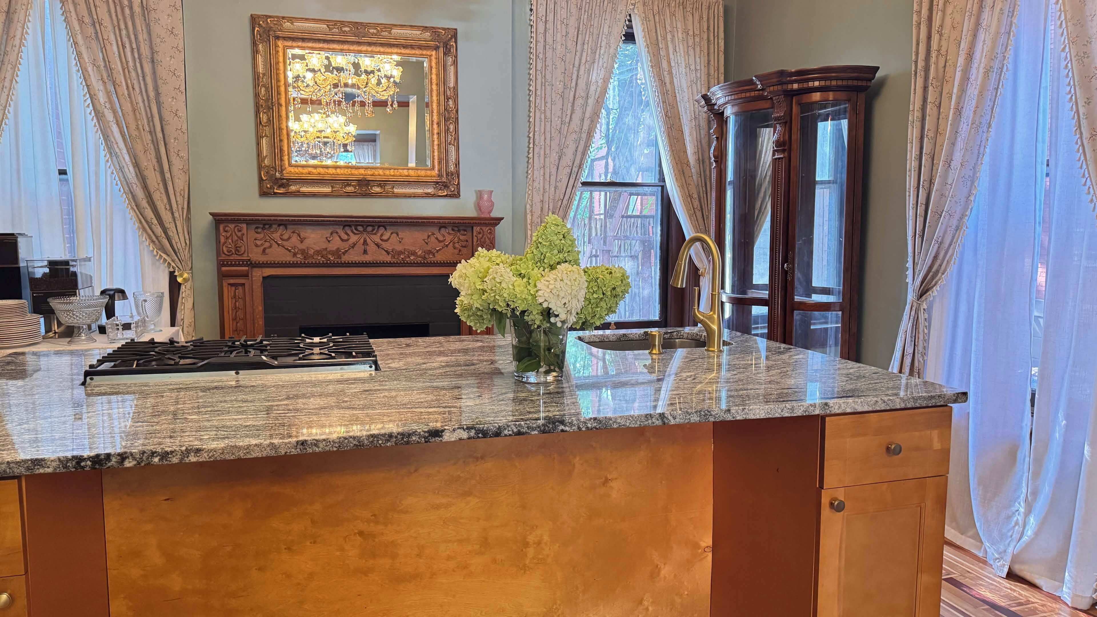 A kitchen with a granite countertop, a gas stove, a vase with flowers, a fireplace, and a large mirror.