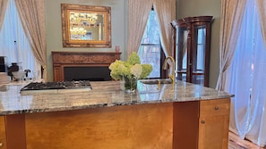 A kitchen with a granite countertop, a gas stove, a vase with flowers, a fireplace, and a large mirror.
