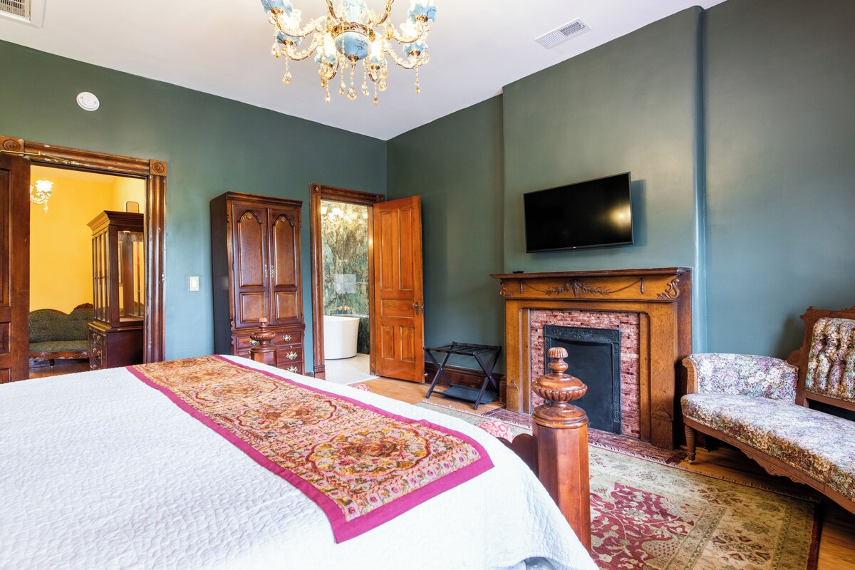 Une chambre à coucher avec un lit, une télévision, une cheminée et un grand miroir.