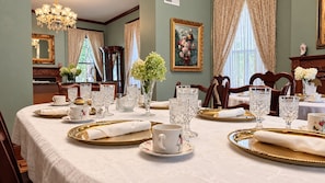 A dining room with a table set for a meal, featuring gold-rimmed plates, clear glassware, and a vase of flowers.