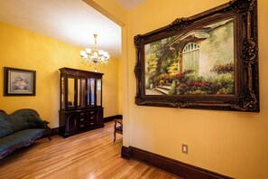 A room with wooden flooring, a green sofa, a wooden cabinet, and a large framed painting on the wall. - Victorian Harvest (Louisville)