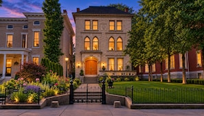 A historic building with a central entrance, a well-maintained garden, and a brick facade.