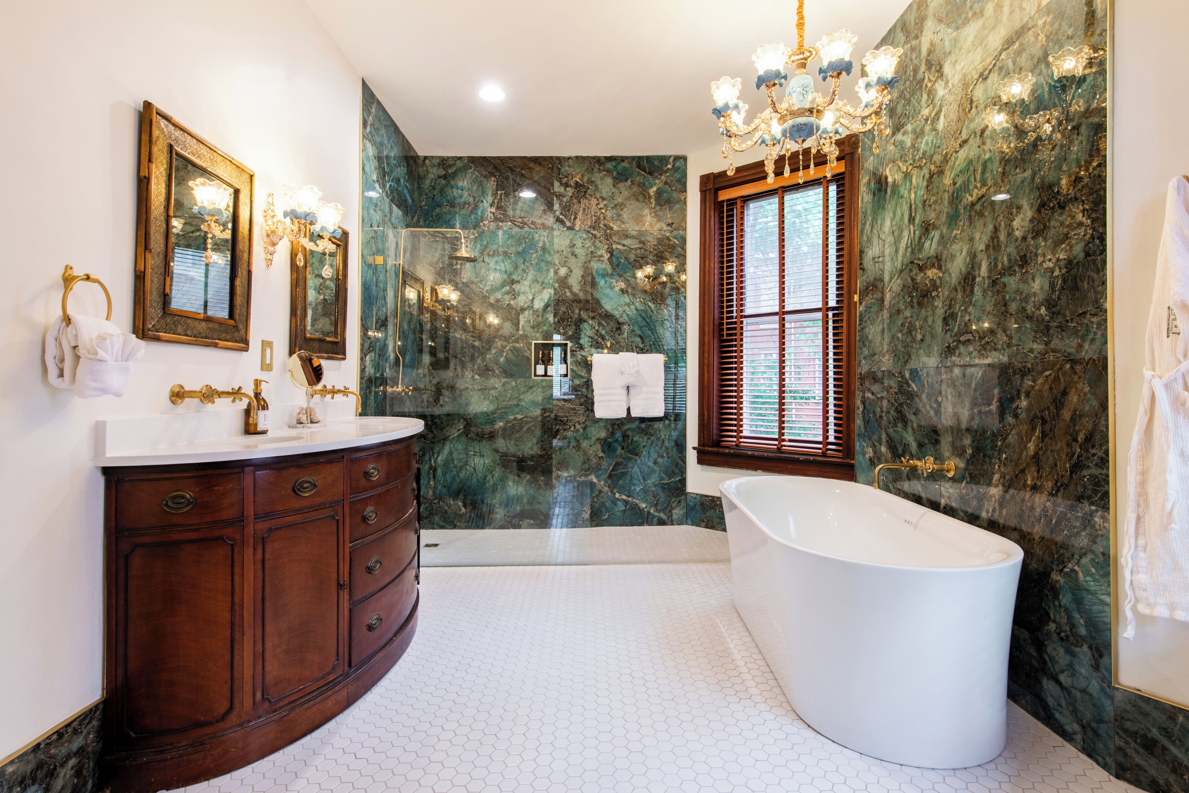 A bathroom with a freestanding bathtub, a vanity with a mirror, and marble walls.