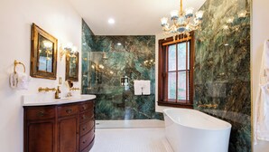 Une salle de bain avec une baignoire sur pieds, un meuble-lavabo avec un miroir et des murs en marbre.