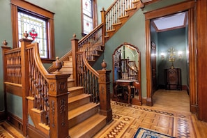 A grand staircase with ornate woodwork, a stained glass window, and a patterned floor. - Victorian Harvest (Louisville)