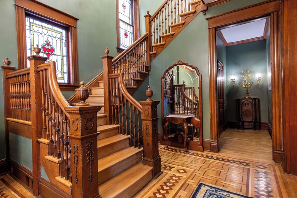 A grand staircase with ornate woodwork, a stained glass window, and a patterned floor. - Victorian Harvest (Louisville)