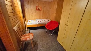 Une petite pièce en bois avec un lit simple, une chaise rouge et une armoire.